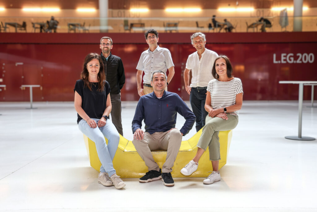 Das Team der Forscher:innen teils sitzend, teils stehend, versammelt um eine der gelben Sitzgelegenheiten in der Halle des Biozentrums: (hintere Reihe, v.l.) Herbert Oberacher, Hesso Farhan, Stephan Geley, (vorne v.l.) Agnieszka Martowicz, Utku Horzum und Margot Haun.