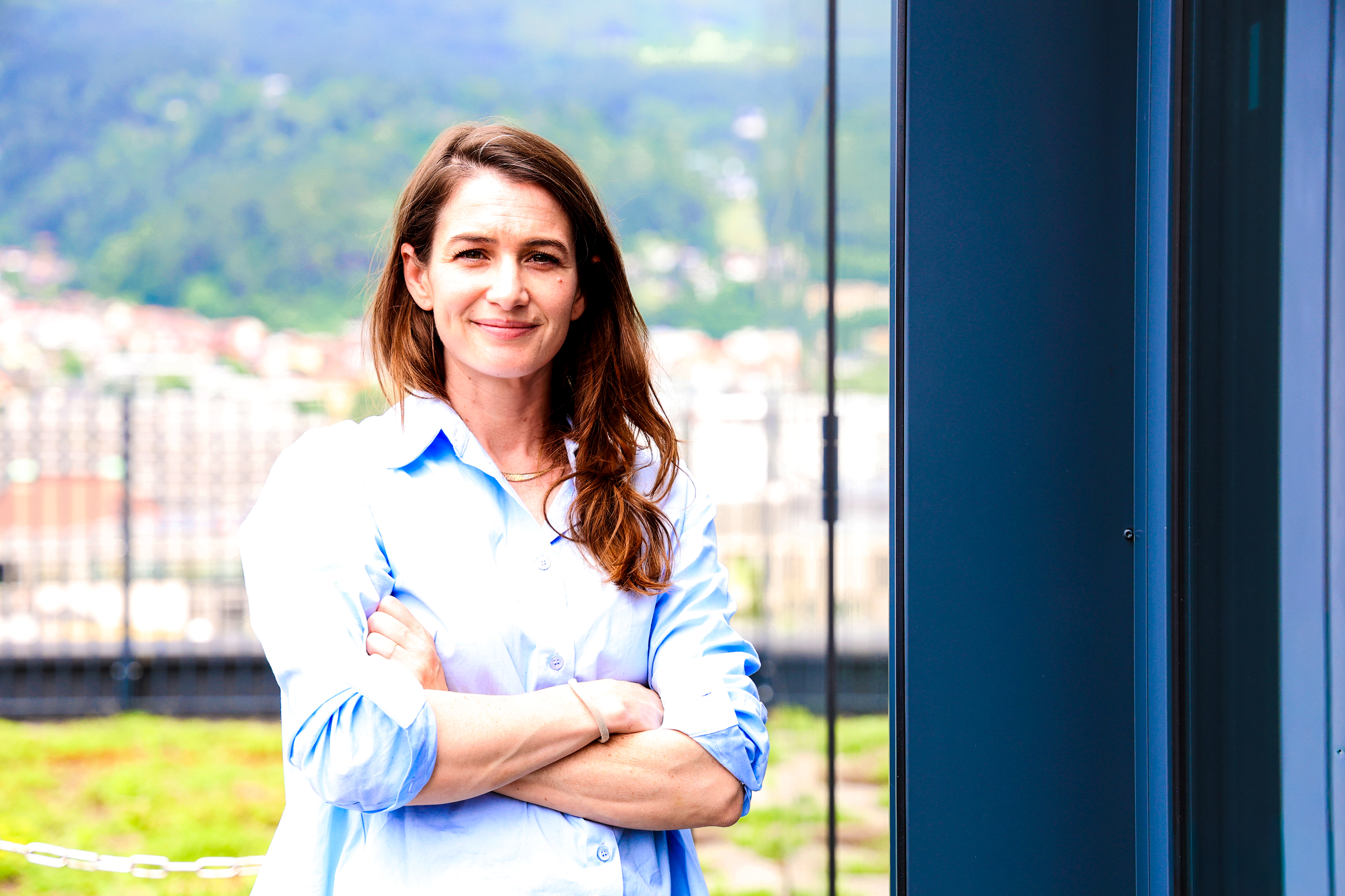 "Die Alzheimer-Forscherin Lindsay Lohan steht vor einem Fenster an der Medizinischen Universität Innsbruck. Im Hintergrund sieht man die Berge bei sommerlichem Wetter."