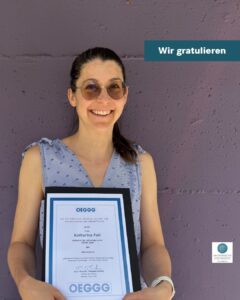 Katharina Feil lächelt in die Kamera und hält ihre Auszeichnung in Händen.